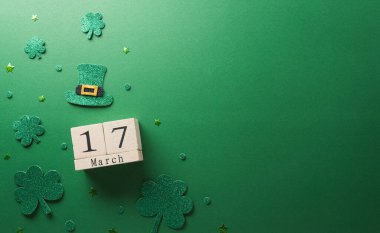 Happy St Patrick's Day decoration concept made from shamrocks ( clover leaf), wooden calendar and leprechaun hat on green background.