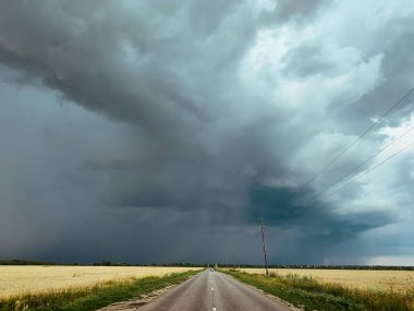 Asfalt yol, rota ve tarlalar üzerinde fırtına bulutları.
