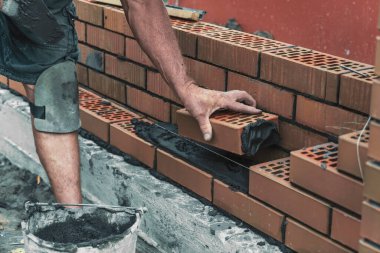 Worker or bricklayer laying bricks. Builder makes brickwork on construction site, close up on hands. clipart