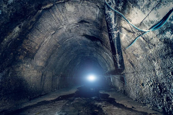 Sewer water in big underground sewage tunnel. Inside dark urban sewerage corridor tunnel with light in end.