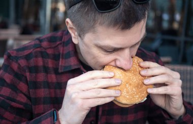 Portrait of hungry man eating burger in city cafe.
