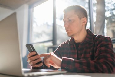 Cheerful freelancer using laptop sitting at table in cafe in sunny day.