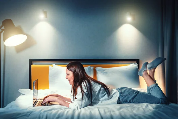 Young woman in bed using laptop. Girl works on Internet, browsing social media or chatting on video call.