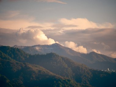 Ağaçlarla kaplı yeşil dağlar doğa manzarası ve gün batımında bulutlar.