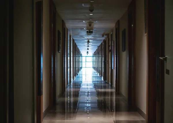 大きな窓から光とドアがたくさんあるホテルの暗い長い廊下 — ストック写真