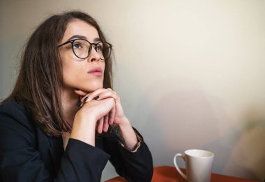 Gözlüklü genç kız evde oturup düşünceli bir şekilde bakıyor. İlham ve yeni fikirler arıyorum. Metin için alanı kopyala.