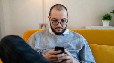 Neşeli genç iş adamı evde telefon kullanıyor. Adam internet üzerinden akıllı telefon üzerinde çalışıyor. Modern yaşam tarzı ve online çalışma konsepti.