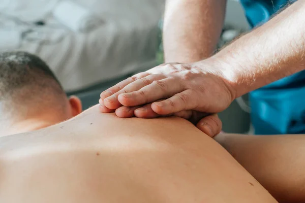 Massage therapist with strong hands and fingers kneads muscles of athlete back shoulder blades after an injury or muscle sprain, therapeutic and pain relieving massage, close up