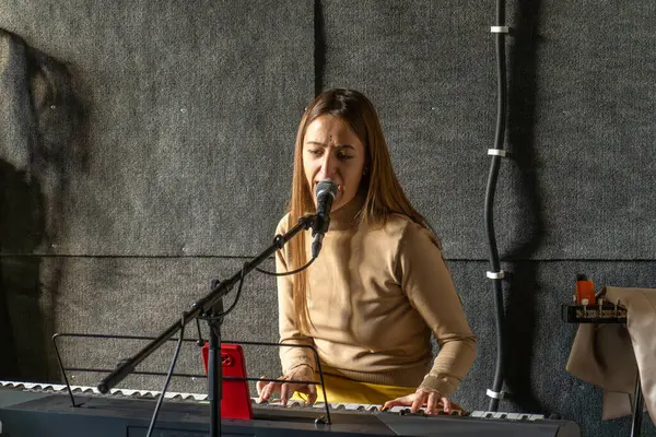 Woman singer play piano and sing in microphone, recording song in sound record studio.