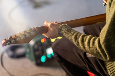 Canlı performanstan önce elektro gitar tellerini ayarlayan gitaristlerin yakın çekimi, sahne ışıkları arka planda hafifçe bulanıklaşır