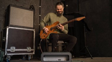 Sandalyede oturmuş, elektro gitar çalıyor. Gitarist ses stüdyosunda sahne sanatlarıyla meşgul..