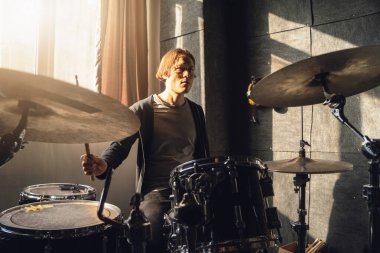 Adam, müzik aletleri ve ekipmanlarıyla çevrili olarak stüdyoda enerjik bir şekilde davul çalıyor. Performansına odaklanmış, ritmik olarak davul çalıyor ve müzik yaratıyor..