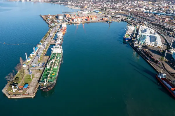 Aerial view of industrial port featuring cargo ships and green tanker, highlighting marine trade and logistics.