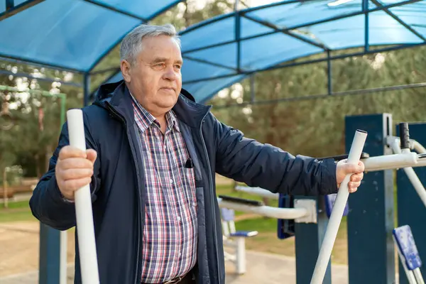 Yaşlı bir beyefendi parktaki spor aletlerini kullanarak fiziksel antrenman yapıyor..