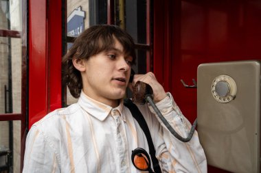 90 'ların tarzında giyinmiş genç adam kırmızı retro eski moda telefon kulübesi ya da şehir sokağında kutu gibi konuşuyor..
