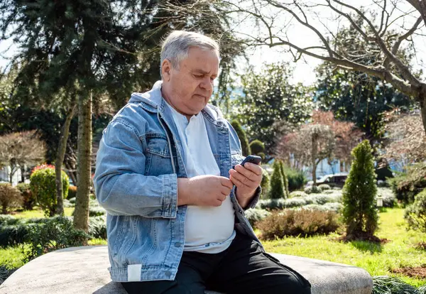 Senior man texting on smartphone while sitting on park bench.