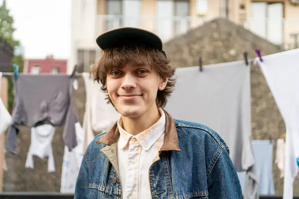 Smiling young man in denim jacket standing in front of hanging laundry.