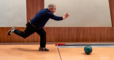 Son sınıf öğrencisi bowling maçında topu fırlatıyor. Enerjik yaşlı adam iş başında, eğlence tesisinde hevesle bowling oynuyor..