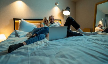 Young couple watches film or content in social media on laptop lying in bed. Time together concept clipart