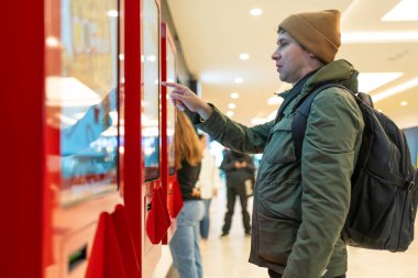 Adam modern alışveriş merkezindeki dijital büfeyle etkileşime geçiyor, dokunmatik ekranda geziniyor. Alışveriş deneyimlerine teknolojik entegrasyon.