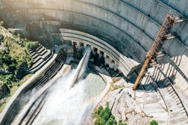 Gürcistan 'daki Inguri hidroelektrik barajı. Güçlü su salınımı, insansız hava aracı görüşü. Yeşilliklerle çevrili büyük mühendislik yapısı yenilenebilir enerji üretimini vurguluyor..