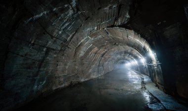 Rutubetli yeraltı beton tüneli kıvrımlı tavanı, ışıkların ışıklarıyla aydınlanıyor..