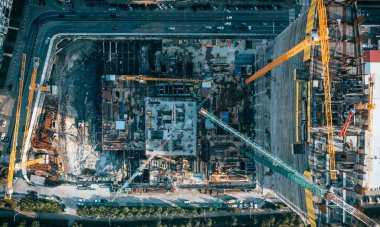 Yoğun kentsel alandaki yollar ve binalarla çevrili, birden fazla vinçli büyük inşaat alanının yukarıdan aşağı görüntüsü.