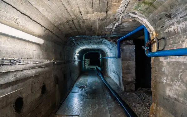 Mavi borular ve elektrik kablolarından oluşan endüstriyel beton tünel gizem ve terk edilme hissi yaratıyor..