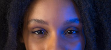 Genç Afro-Amerikan kadın gözlerinin yakın çekimi, doğal ve mavi ışıkla aydınlatılmış..