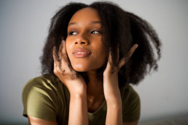 Kıvırcık saçlı, ellerinde dinlenen çenesi olan genç Afrikalı Amerikalı kadın dikkatlice yukarı bakıyor. Işık arka planına karşı derin düşüncelere ve sükunete kapılır..