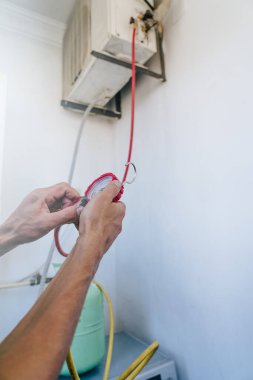 Teknisyen klimayı tamir ediyor ve yaz sıcağına hazırlanmak için onu freonla dolduruyor. Basınç göstergesini ayarlayan ve hortumları açık hava ünitesine bağlayan ellere yakın çekim. HVAC bakımı ve