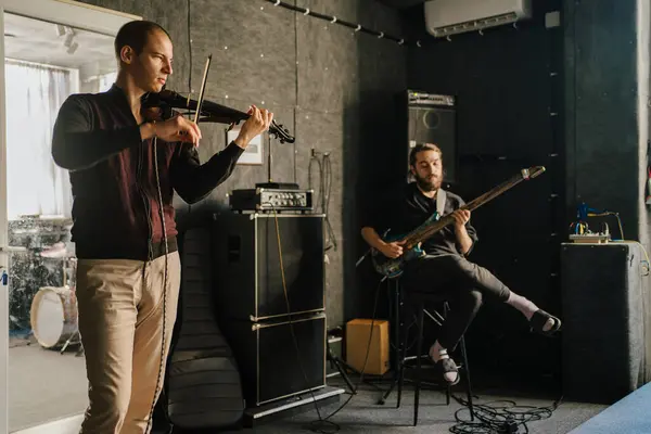 stock image Musicians playing violin and bass guitar in recording studio. Focused performers practicing together, surrounded by professional equipment. Music production, rehearsal, and band practice themes.