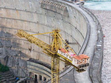 Yellow crane on Enguri dam in Georgia. Industrial equipment stands against massive concrete structure, aging machinery and infrastructure maintenance. clipart