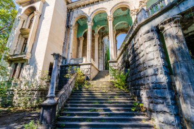 Yıpranmış eski taş basamaklar ve aşırı gelişmiş bitki örtüsü tarihi, terk edilmiş uzun kemerli ve klasik mimarili bir binaya götürür..