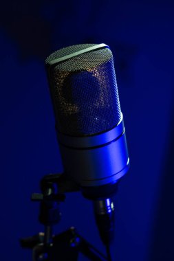 Stüdyo yoğunlaştırıcı mikrofonu koyu mavi arkaplana yakın plan, dokuyu ve profesyonel ses ekipmanlarını vurguluyor.