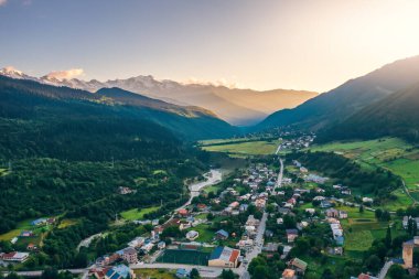 Gürcistan 'ın Svaneti kentindeki manzaralı dağ köyü, yemyeşil çayırları, kıvrımlı nehri ve ılık altın ışıkta karla kaplı zirveleri var..