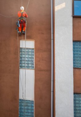 Industrial climber hanging on ropes near modern building facade during maintenance work. clipart