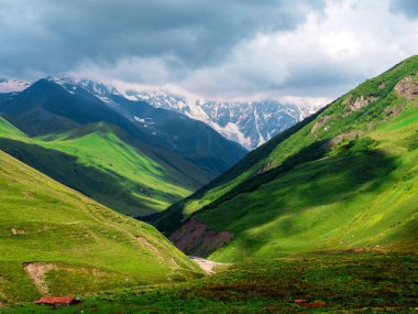 Gürcistan 'ın Svaneti kentindeki yemyeşil dağların panoramik manzarası. Manzaralı tepe ve vadilerin üzerindeki dramatik bulutlar bölgenin nefes kesici doğal güzelliklerini gözler önüne seriyor..