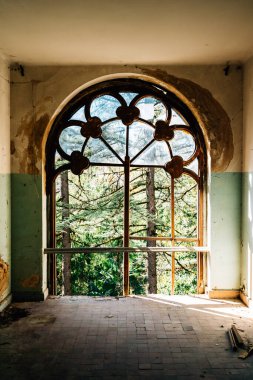Terk edilmiş malikanenin eski vitrinleri, soyulmuş boyalar ve dışarıda görülebilen ağaçlar, nostalji ve tarihsel çürümeyi çağrıştırıyor..
