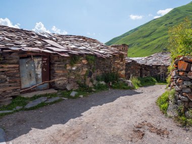 Georgia 'nın Svanetian köyünde otantik kırsal mimari. Geleneksel taş ev ahşap elementler ve çitlerle çevrili yol yemyeşil dağlar ve açık mavi gökyüzü ile çevrili..