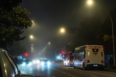 Batumi şehir caddesinde sisli bir gece, parlayan sokak lambaları, sisli hava, yolda arabalar ve elektrikli otobüsler, şehir ulaşımı, toplu taşıma, gizemli hava, sis, çevre ve modern hava