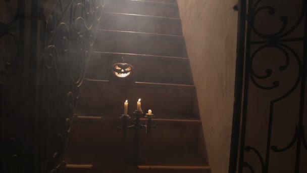 ホラーハロウィンのコンセプト 不気味な放棄された城 古い燭台とハロウィーンのカボチャは 夜に格子ドアで木製の階段に輝く バックライトと霧で装飾 選択的焦点 — ストック動画