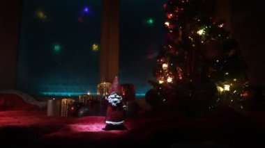 Noel ve Yeni Yıl kavramı. Kırmızı halıda dikilen fidan ağacı geleneksel tatil özellikleriyle. Arka planda renkli ışıklar olan rahat bir pencere. Seçici odak