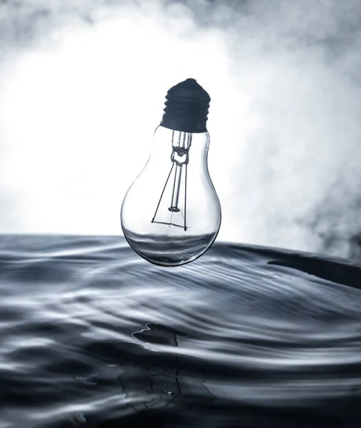 Abstract concept. Light bulb dropping on water or water splash on dark foggy background. Selective focus.