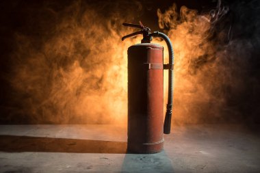 Yangın koruma konsepti. Karanlık sisli arka planda, ışıklı eski bir yangın söndürücü. Seçici odak