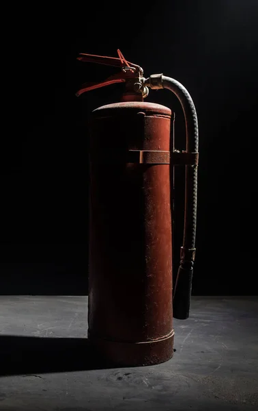 Fire protection concept. Old fire extinguisher on dark foggy background with light. Selective focus