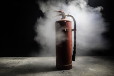 Yangın koruma konsepti. Karanlık sisli arka planda, ışıklı eski bir yangın söndürücü. Seçici odak