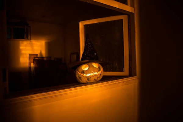 Scary Halloween pumpkin in the mystical house window at night or halloween pumpkin and horror silhouette in window. Selective focus