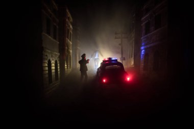 Gece polis baskını ve sen tutuklusun. Arka tarafta polis arabasının silueti var. Görüntü sisli arka planda yanıp sönen kırmızı ve mavi polis ışıkları.