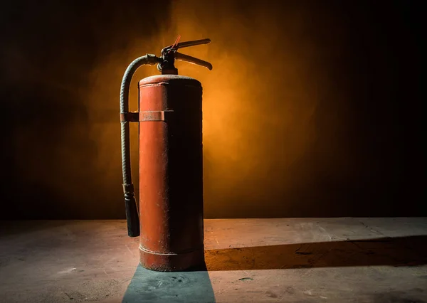 Fire protection concept. Old fire extinguisher on dark foggy background with light. Selective focus